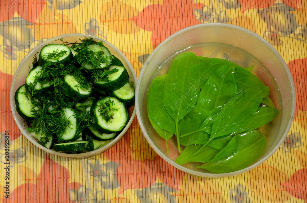 Obraz premium Two plastic bowls-one with sliced ​​cucumber with dill, the second with spinach in the water.