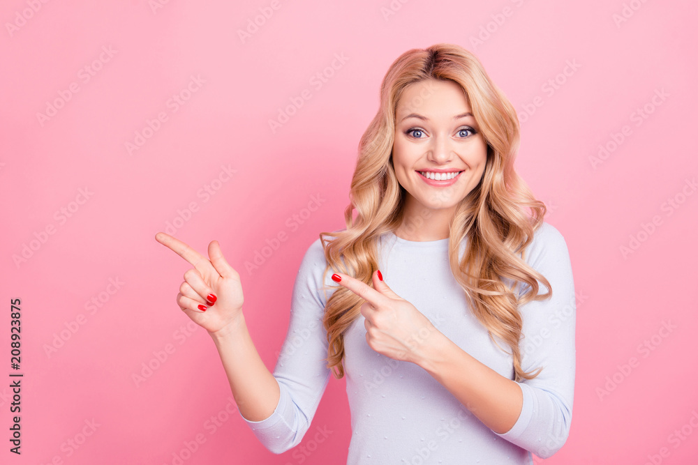 Fototapeta premium Portret uroczej zębatej dziewczyny w swetrze z promiennym uśmiechem wskazującym dwoma palcami wskazującymi na puste miejsce, patrząc na aparat odizolowany na różowym tle