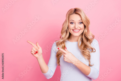 Portrait of charming toothy girl in pullover with beaming smile pointing two forefingers to copyspace empty place looking at camera isolated on pink background