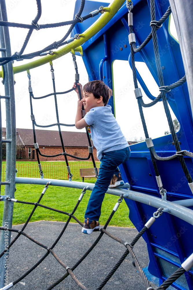 A young boy climbing on a rope net on a climbing frame in a playground. A young boy climbing on a rope net on a climbing frame in a playground.