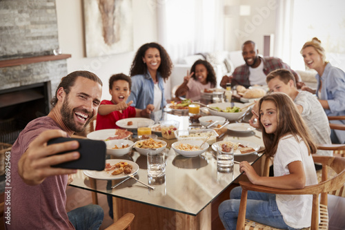 Two Families Taking Selfie As They Enjoy Meal At Home Together