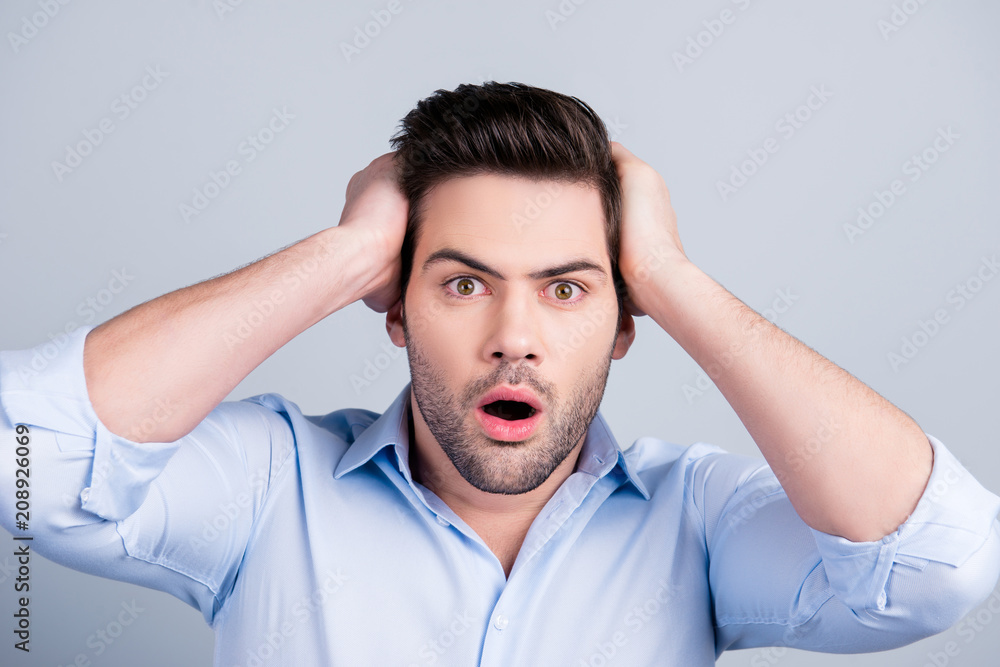 Portrait of surprised shocked man with stubble and wide opened mouth in shirt touching head with two hands isolated on grey background Portrait of surprised shocked man with stubble and wide opened mouth in shirt touching head with two hands isolated on grey background