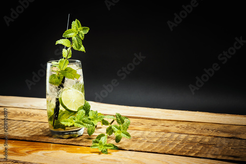 glass of delicious mojito with lime and mint leaves on a wooden table on a black background