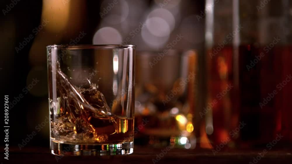 Super slow motion of falling ice cube into whiskey glass. Filmed on cinema slow motion camera, 1000fps Super slow motion of falling ice cube into whiskey glass. Filmed on cinema slow motion camera, 1000fps