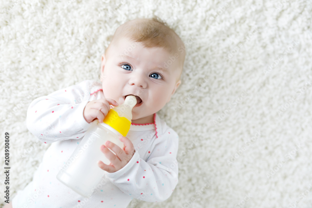 Cute adorable ewborn baby girl holding nursing bottle and drinking formula milk Cute adorable ewborn baby girl holding nursing bottle and drinking formula milk