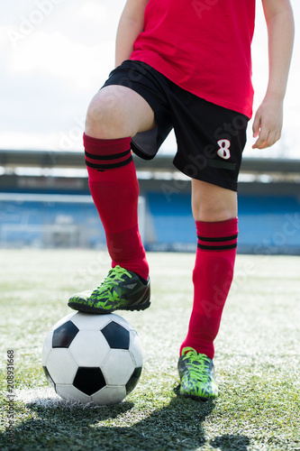 Fototapeta Naklejka Na Ścianę i Meble -  Low section portrait of unrecognizable teenage boy wearing red uniform standing on football field and stepping on ball