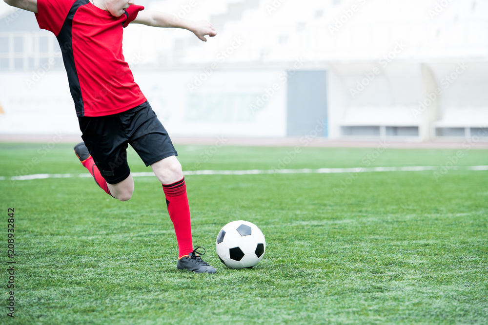 Portrait of unrecognizable teenage boy kicking ball playing football on stadium during practice, copy space