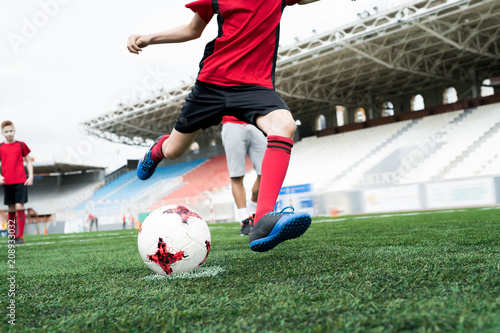 Low section portrait of unrecognizable teenage boy kicking ball forcefully playing football on stadium during practice, copy space