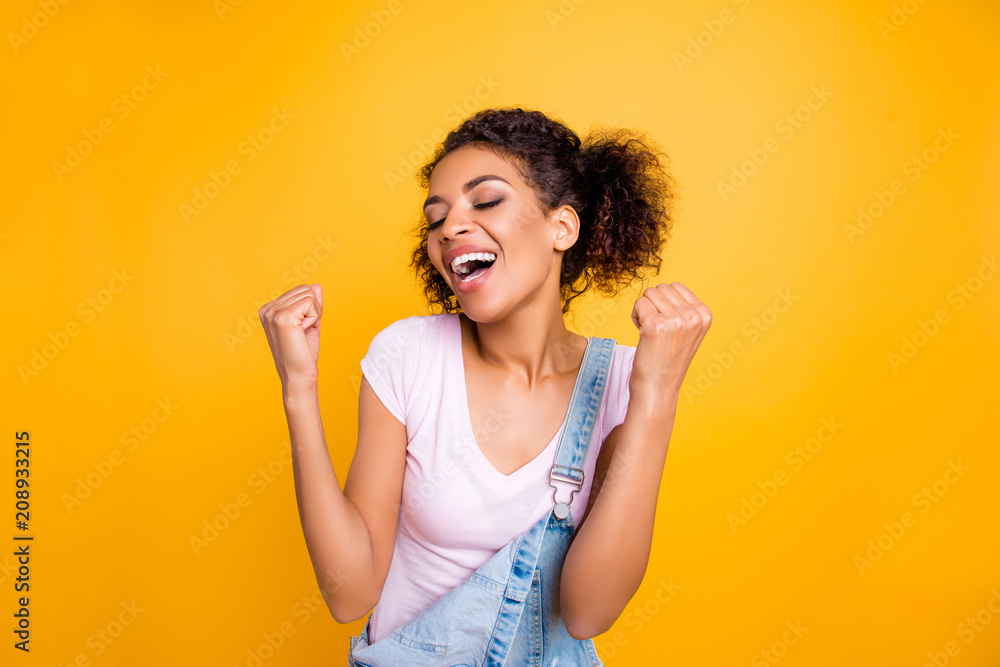 Portrait of cheerful fancy girl in white t-shirt keeping eyes closed with raised arms celebrating victory isolated on yellow background Portrait of cheerful fancy girl in white t-shirt keeping eyes closed with raised arms celebrating victory isolated on yellow background