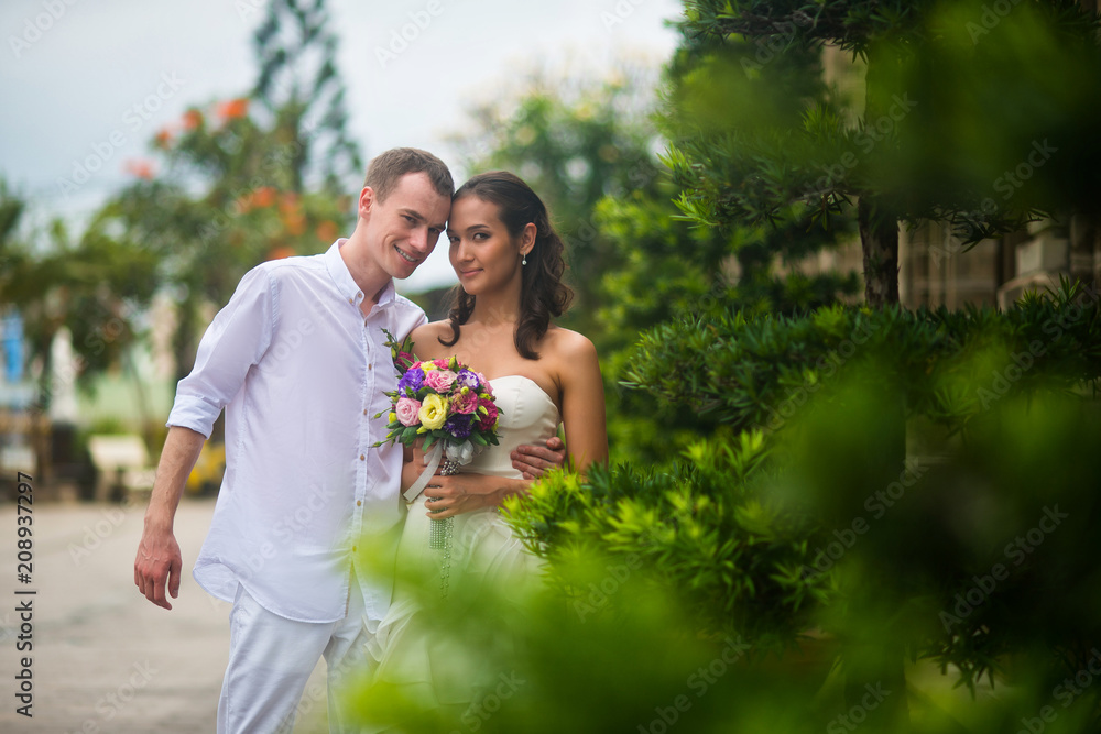 Naklejka premium a wedding couple, a beautiful young bride and groom, are standing in the Park outdoors, embracing and and smiling