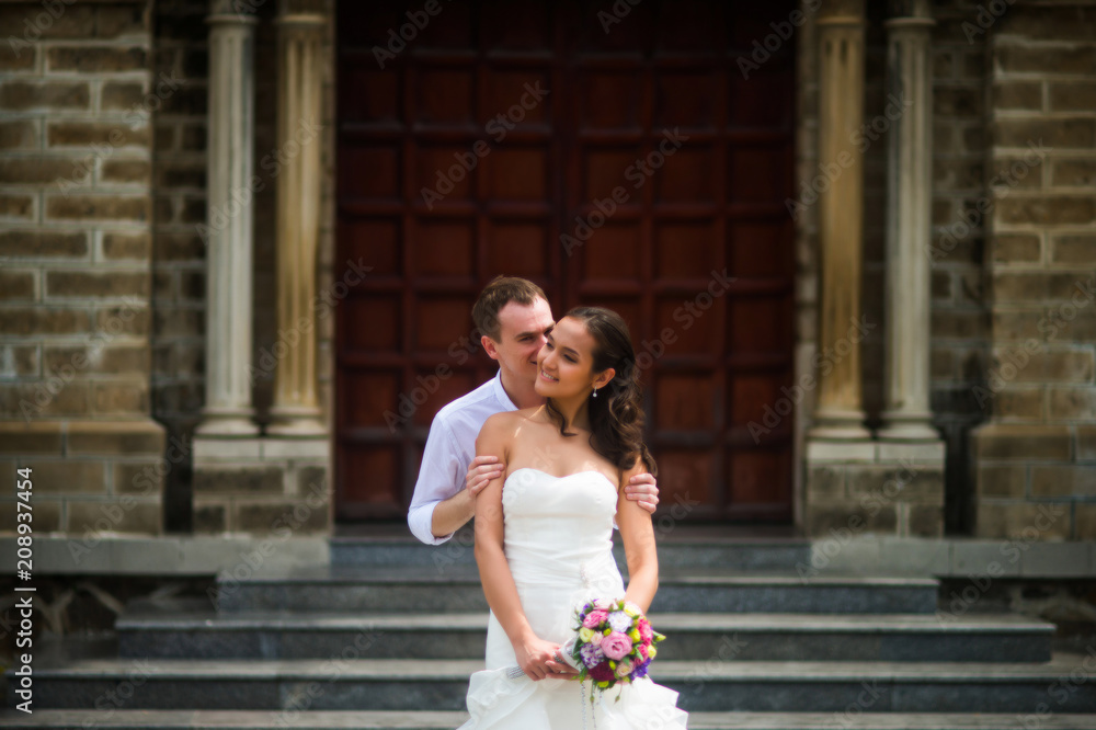 Naklejka premium The groom kisses the bride against the Catholic Church