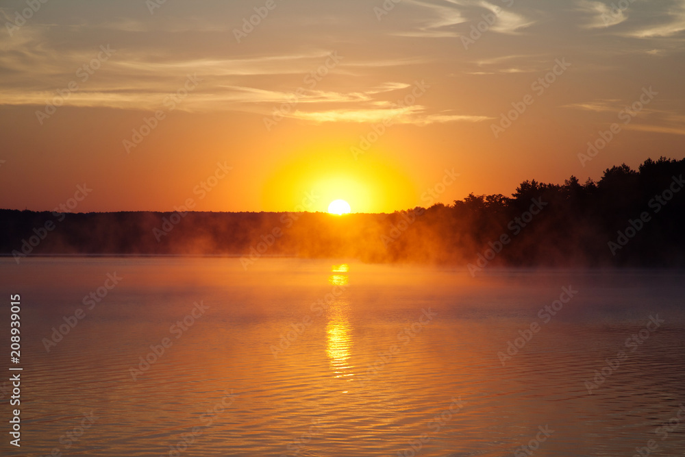 Beautiful sunrise on the lake. Early morning landscape. mist on the water, forest silhouettes and the rays of the rising sun.
