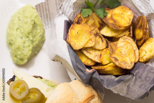 Delicious beef burger with plantain chips and guacamole on a newspaper