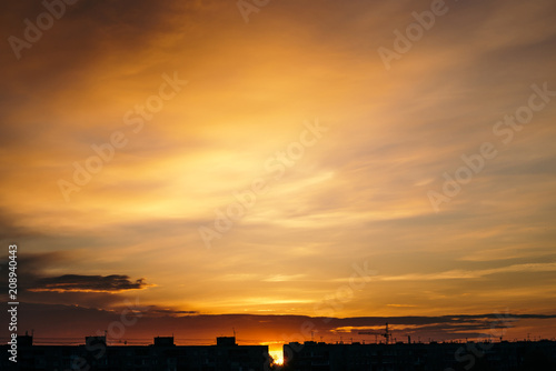 Beautiful cloudy dramatic morning sky above silhouette of city buildings. Picturesque dawn in city. Background of varicolored clouds. Unimaginable fantasy sunrise in heaven.