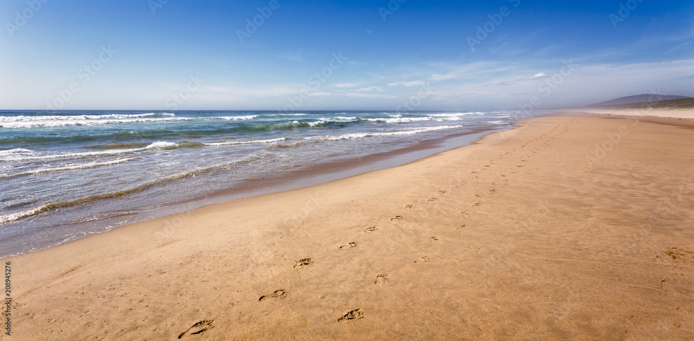 Water lapping on long sandy beach on hot summers day with foorprints leading into the distance