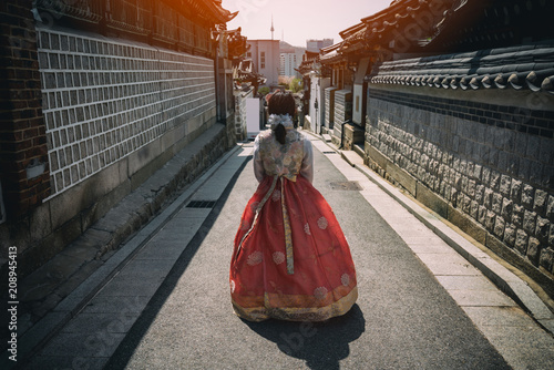 Young woman traveler in traditional korean dress or call hanbok traveling into  Bukchon Hanok Village with N Seoul Tower on Namsan mountain in background at Seoul, South Korea. photo