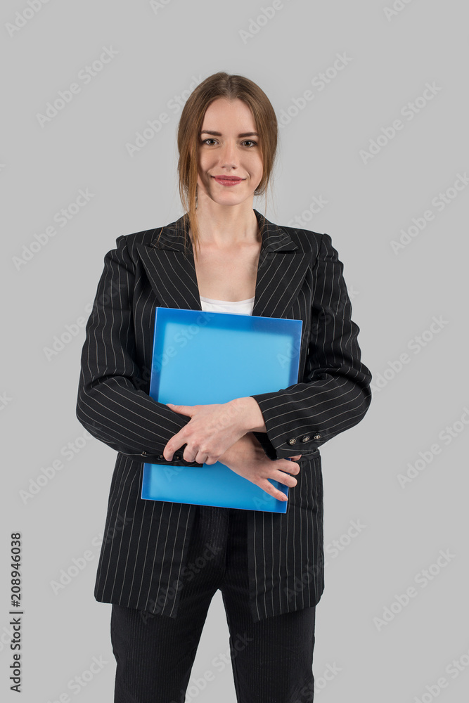 young successful woman in a strict dark suit with a blue file in hands looking at camera and smiling young successful woman in a strict dark suit with a blue file in hands looking at camera and smiling