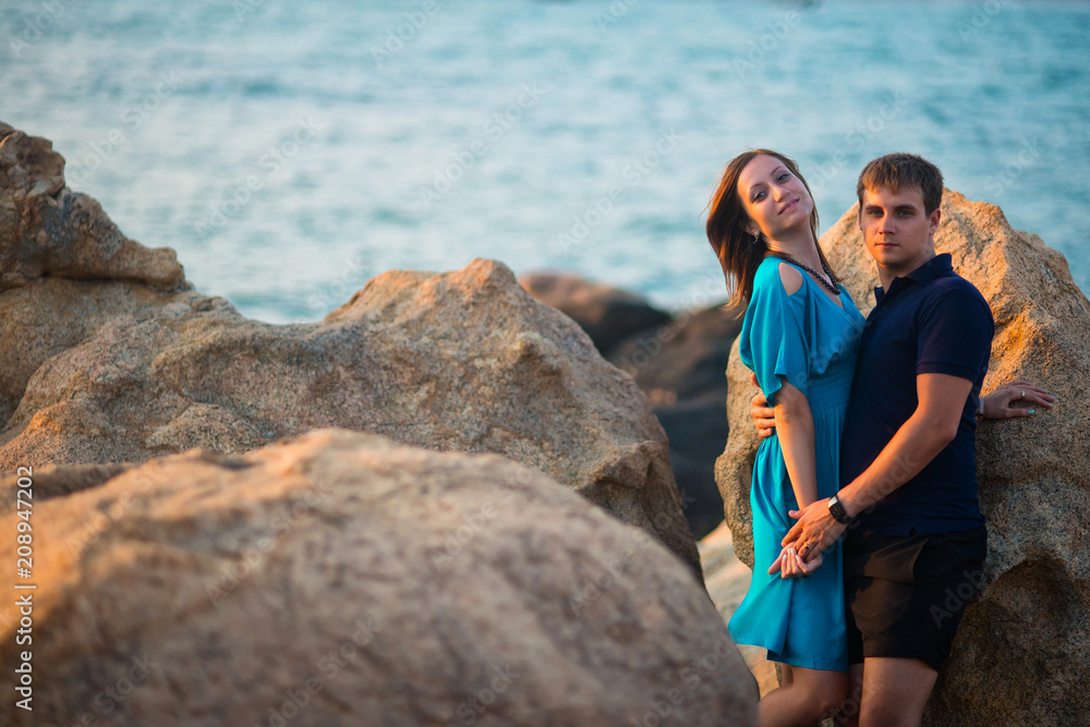 Young couple standing in the middle of large boulders on the background of the sea Young couple standing in the middle of large boulders on the background of the sea