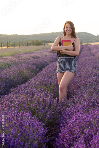 Fototapeta Naklejka Na Ścianę i Meble -  Beautiful young woman is on the lavender field with books