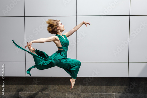 Beautiful girl dancing in the city and jumping against the wall background.