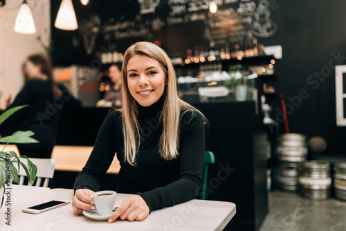 Smiling blonde woman sitting in the modern cafe bar. Looking at camera.