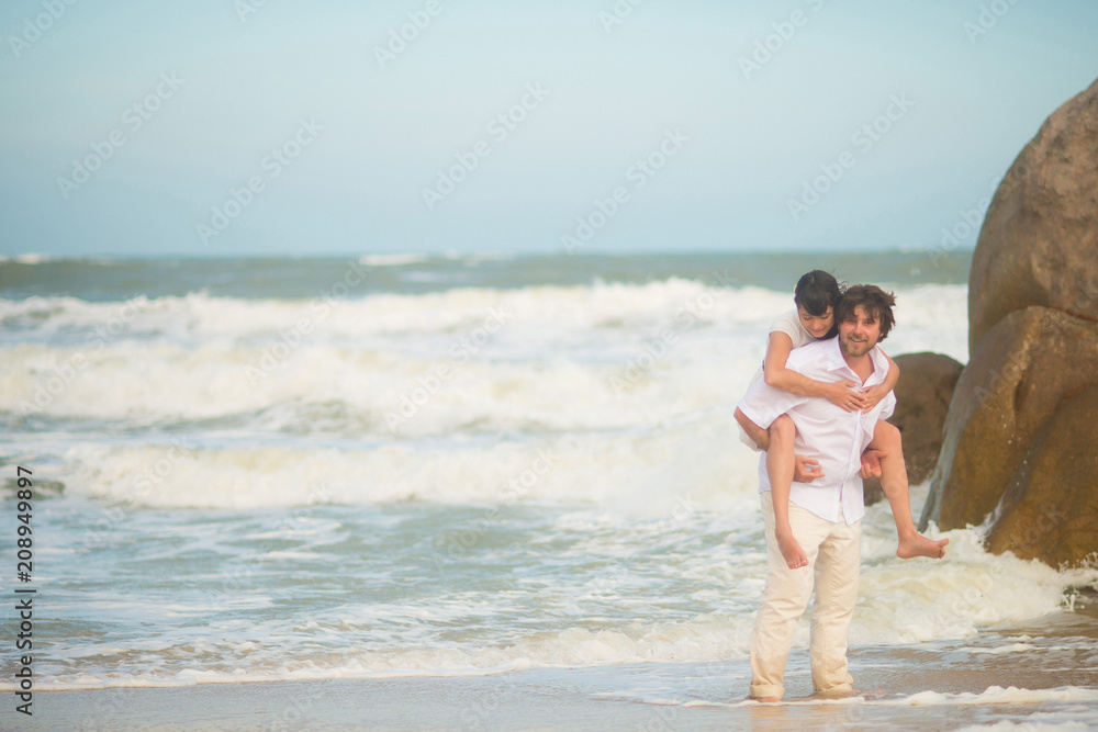 The groom carries the bride on his back against the sea and rocks