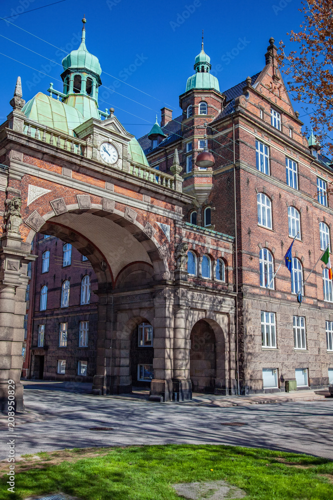 beautiful historical building with archway, clock and flags in copenhagen, denmark