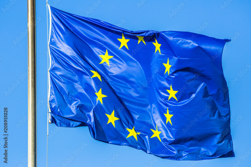 Flag of Europe blue color with yellow stars waving in the wind on blue sky.  Photos | Adobe Stock