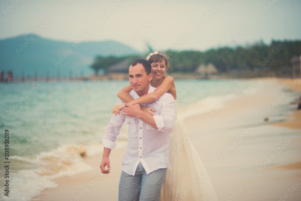 The bride hugs the groom from behind on the beach The bride hugs the groom from behind on the beach