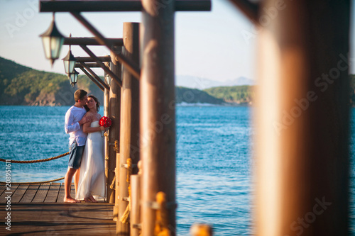 Wedding couple kissing on the pier near the lampposts in the tropics against the sea