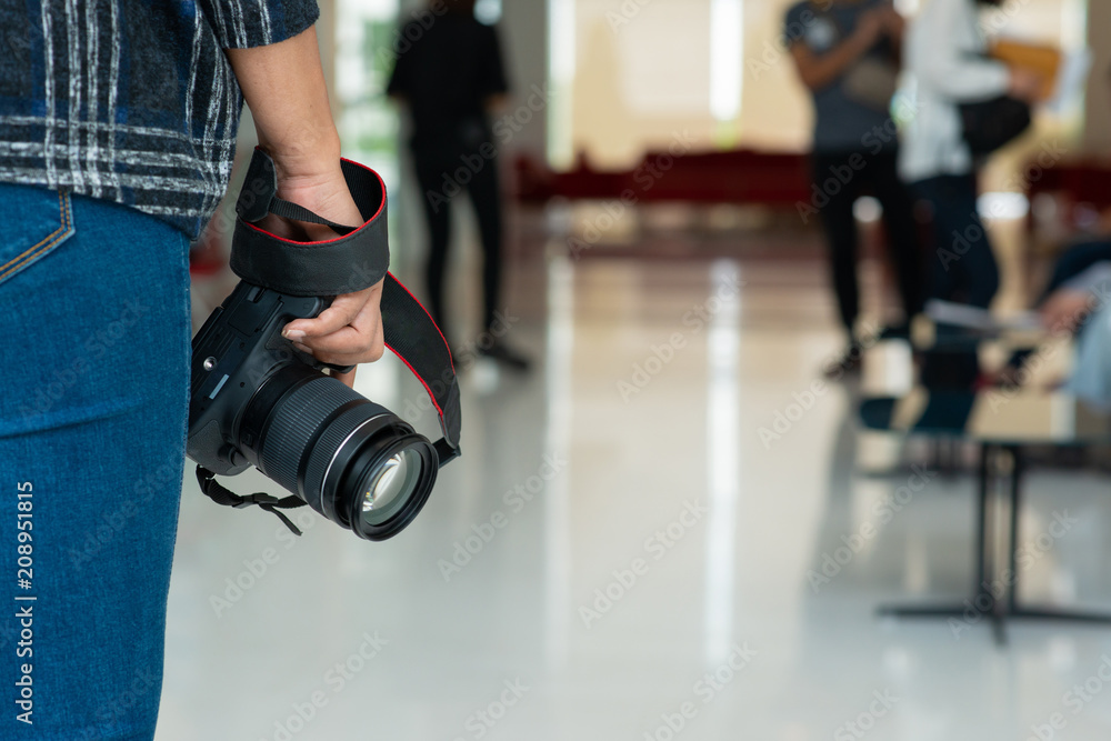 Fototapeta premium Rear view of a female photographer with a modern DSLR camera in her hand against a blurred crowded street