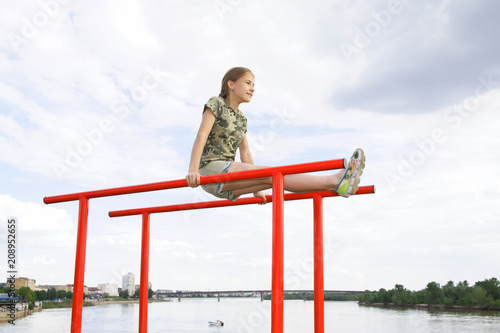 Obraz na płótnie Smiling teenage girl doing gymnastic exercises on uneven bars in city conditions outdoors w salonie