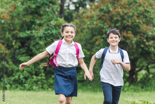 happy schoolchildren with backpacks running by park