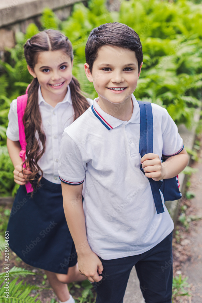 happy schoolchildren with backpacks looking at camera in park happy schoolchildren with backpacks looking at camera in park