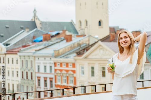 Young woman enjoying great view standing on the terrace of restaurant with soft drink glass..Travel, tourism and resting concept.