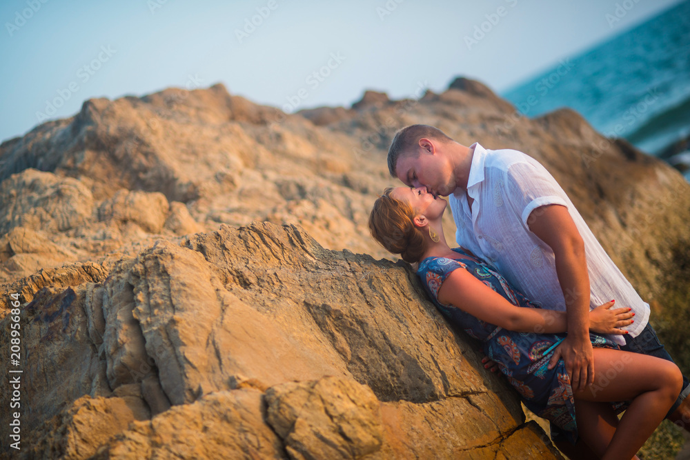 Cute couple kissing in the rocks at sunset against the ocean