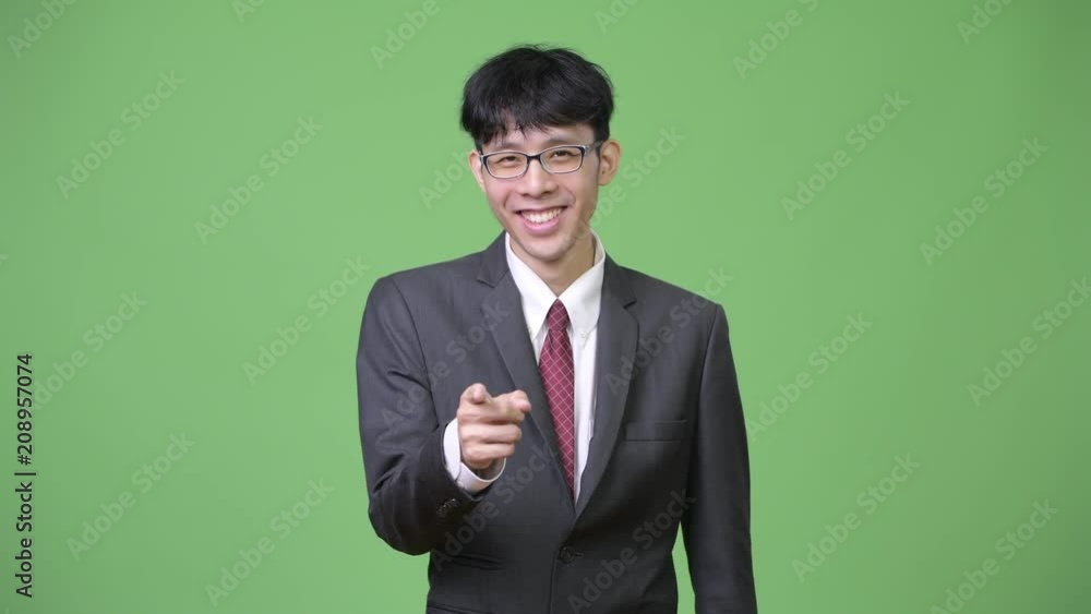 Young happy Asian businessman smiling while pointing to camera Young happy Asian businessman smiling while pointing to camera