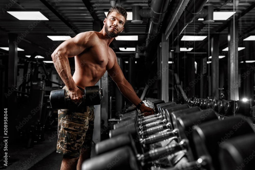 Male athlete lifts dumbbell near counter opposite mirror in gym. Concept workout, bodybuilder. Male athlete lifts dumbbell near counter opposite mirror in gym. Concept workout, bodybuilder.