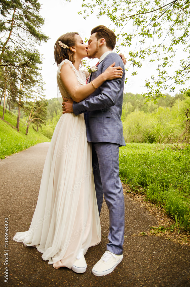 Naklejka premium Bride and groom hugging and kissing, standing on the path in the background of nature