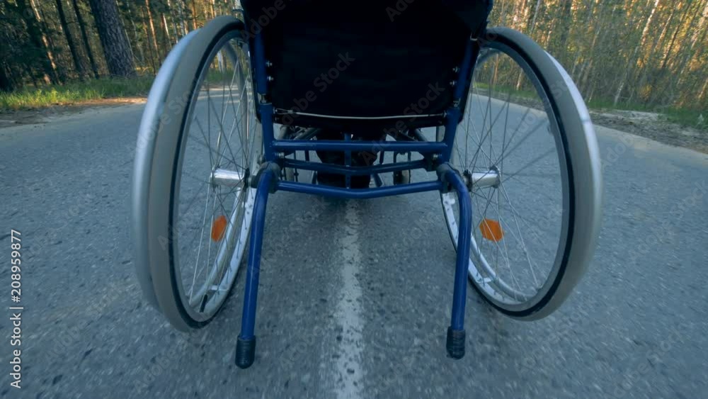 Back view of a moving training wheelchair with a disabled man in it Back view of a moving training wheelchair with a disabled man in it