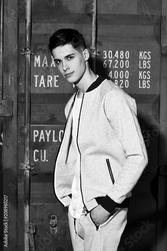 Young handsome sporty man in gary sport clothes posing against red metal doors of intermodal container photo