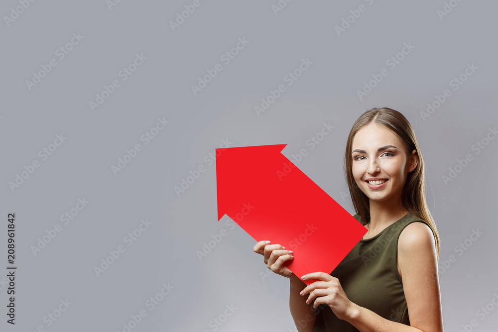 Young beautiful woman holding a big red arrow pointing upwards Young beautiful woman holding a big red arrow pointing upwards