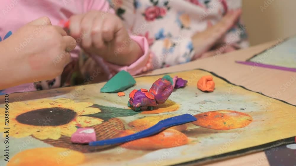 Unknown little girl sitting at the desk sculpts a different figures from made of colored modeling plasticine in the nursery. Development of the art of modeling in children Unknown little girl sitting at the desk sculpts a different figures from made of colored modeling plasticine in the nursery. Development of the art of modeling in children