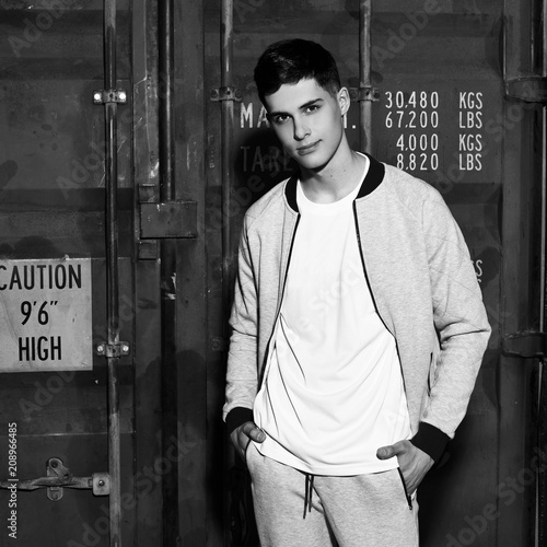 Young handsome sporty man in gary sport clothes posing against red metal doors of intermodal container photo