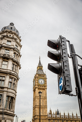 Vertical view of a traffic light with the Big Ben Clock Tower and a old building in the background. London