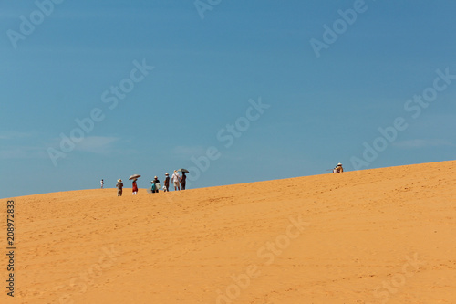 Group of tourists with umbrellas in desert landscape / red sand dune in Mui Ne, Vietnam