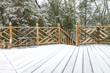 Empty wooden deck of house with statue decorations, chairs, staircase down on backyard in neighborhood with snow covered wood floor during blizzard white storm, snowflakes falling in Virginia suburb