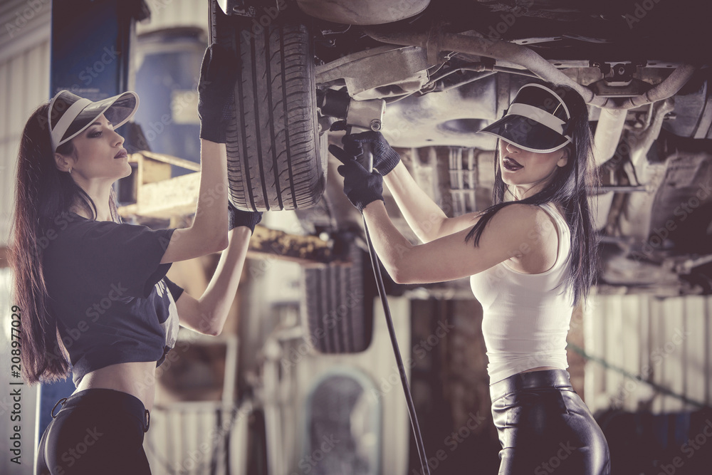Two women mechanics are repairing a car on the lift.