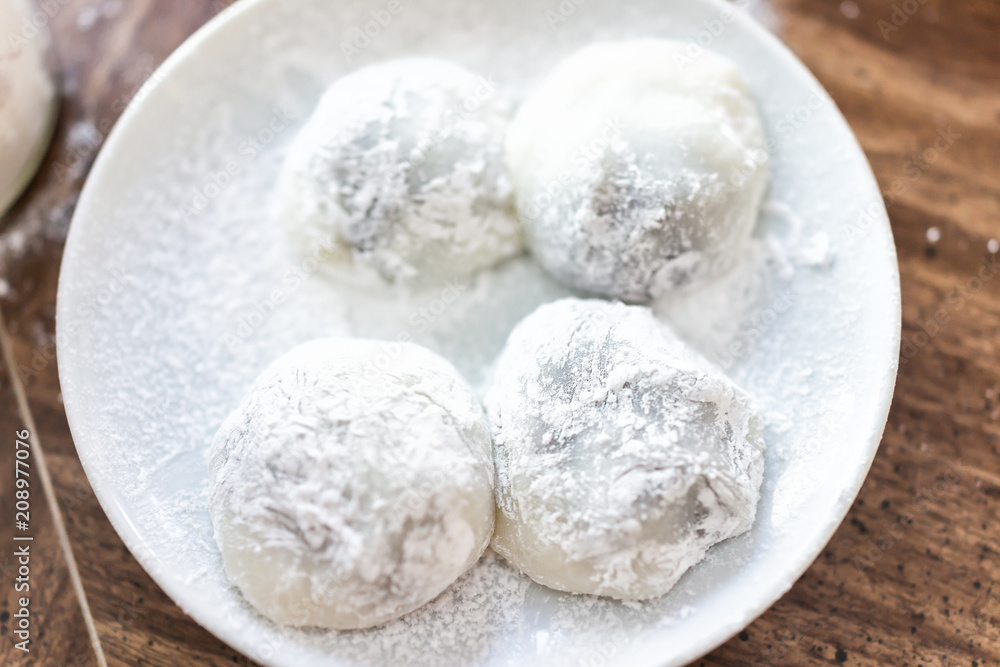 Four round whole mochi sticky glutinous rice cake dessert pieces, wagashi daifuku filled with red bean adzuki jam filling flat top view on plate, table
