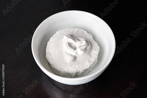 Cottage cheese in white ceramic bowl covered sour cream on the dark wooden table. Curd - dairy, fermented milk product